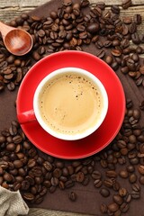 Obraz premium Cup with aromatic coffee, beans and napkin on wooden table, flat lay