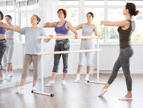 Adult female teacher showing ballet moves to group of beginner women in studio