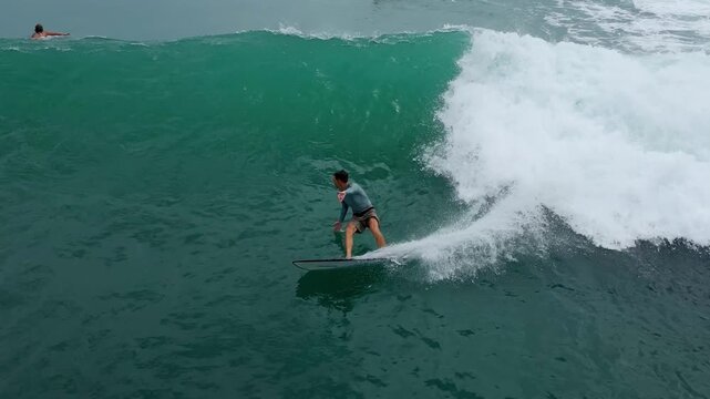 Aerial Surfer Riding Emerald Wave, Carving Powerful Turn Along Reef Break With Cascading Whitewater And Spray,