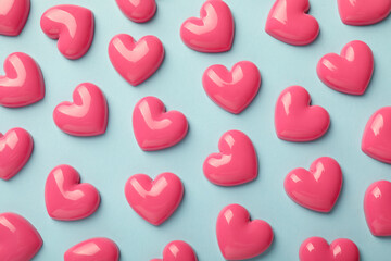 Fototapeta premium Pink decorative hearts on light blue background, flat lay