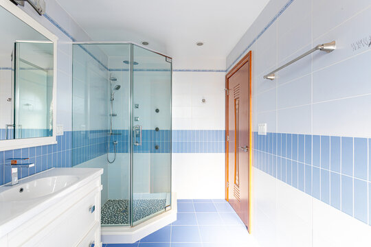 Bright bathroom interior with glass corner shower, blue and white tile walls, vanity sink, and wooden door in residential home