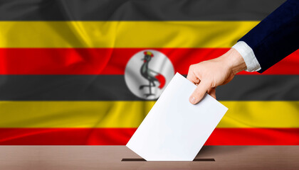 Uganda presidential vote 2026. Hand placing a ballot in ballot box with the Ugandan flag in the...
