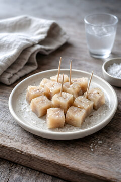 Icelandic fermented shark h&aacute;karl served on a minimalist ceramic plate with sea salt on rustic wood. Nordic food photography with soft natural daylight and cool tones, authentic documentary style.