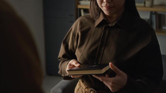 Unknown spiritual guide giving bible book in leather cover to young woman who examining it and thanking man