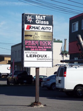 
Ottawa, ON, Canada-July 8,2025: A commercial sign in Ottawa features "M&T Glass, KMAC Auto, Al Zain Auto, Pride Rock Granite, and Leroux Sharpening services" on Michael Street.