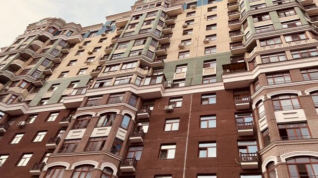 Low angle view stylish residential facade with ornate balconies, brick base, stacked windows under blue sky, warm cinematic grading, detailed cornices and repeating vertical rhythm, closeup