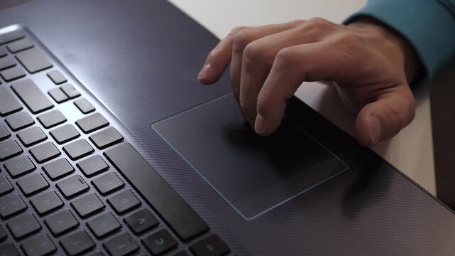 Closeup hand on laptop touchpad navigating cursor with light gestures, fingers poised above keyboard, modern dark laptop surface, indoor desk, remote work mood, focused movement and precise control