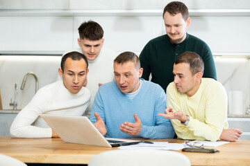 Several male friends solve problems using laptop and internet at home