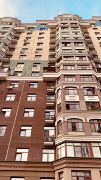 Low angle view stylish residential facade with ornate balconies, brick base, stacked windows under blue sky, warm cinematic grading, detailed cornices and repeating vertical rhythm, closeup