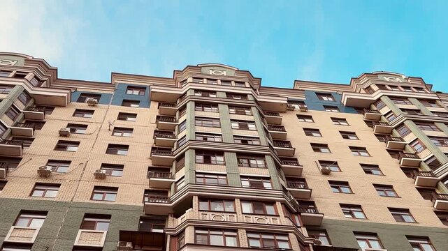 Low angle view stylish residential facade with ornate balconies, brick base, stacked windows under blue sky, warm cinematic grading, detailed cornices and repeating vertical rhythm, closeup