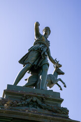 Obraz premium Classical statue of Diana the Huntress in Praza Galicia Fonte de Diana, Betanzos, Galicia, Spain. Historic stone fountain surrounded by lush greenery.