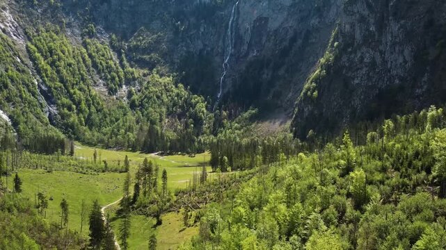 Majestic waterfall cascading down steep rocky cliff ito green alpine valley aeral view