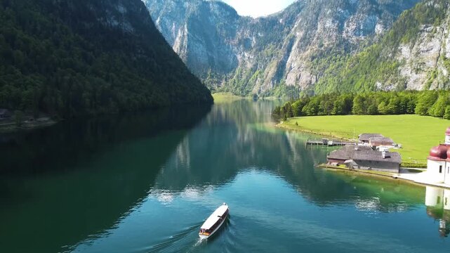 Electric tourist boat crossing the emerald waters of ake K&ouml;nigssee surrounded b mountains aerial view