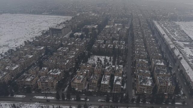 A drone shot of Aleppo, Syria, during a heavy snowstorm shows urban architecture and streets covered in white. Cinematic winter scenery in a Middle Eastern urban environment.