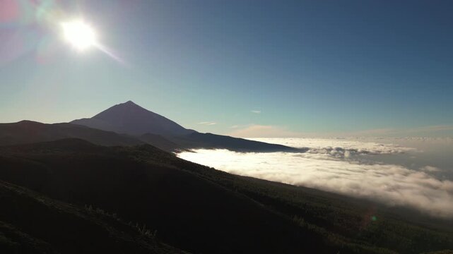 A lone mountain peak pierces a sea of clouds under a bright sun.