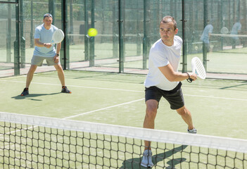 Obraz premium Men play padel on an outdoor tennis court. Hitting the ball with a racket