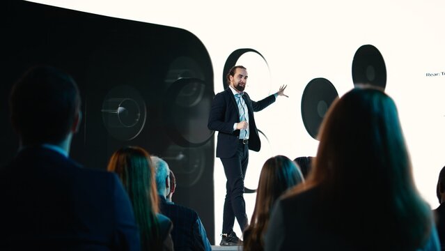 Male CEO presenting new mobile phone product launch on stage with premiere of modern smartphone interface. Entrepreneur introduces innovation and development with product release. - Powered by Adobe