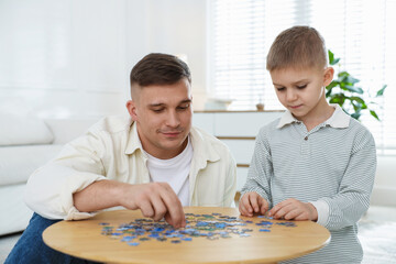 Fototapeta premium Father and his son solving jigsaw puzzle at home