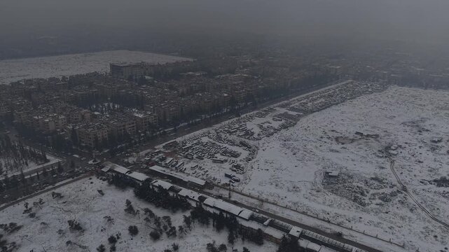A drone shot of Aleppo, Syria, during a heavy snowstorm shows urban architecture and streets covered in white. Cinematic winter scenery in a Middle Eastern urban environment.