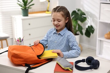 Girl packing her backpack for school at desk indoors