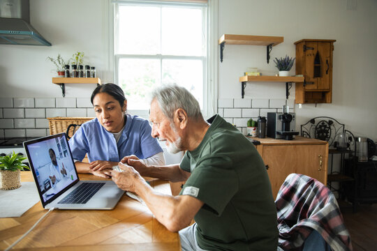 Senior man and nurse having telehealth consultation at home kitchen table
