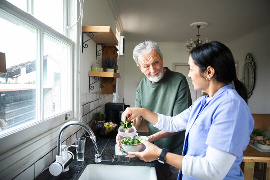 Caregiver helping senior man prepare a healthy meal in home kitchen