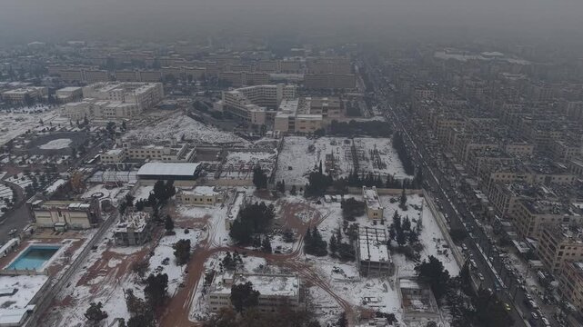 A drone shot of Aleppo, Syria, during a heavy snowstorm shows urban architecture and streets covered in white. Cinematic winter scenery in a Middle Eastern urban environment.