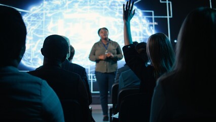 Girl in audience interacting with black female speaker presenting AI systems at business convention, showing automation and AI brain visuals for software development. Active participants.