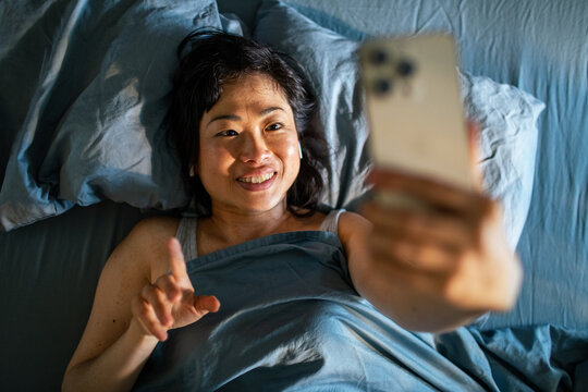 Smiling woman video chatting on smartphone in bed at home