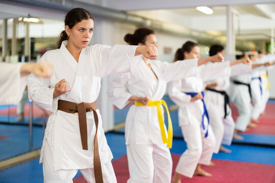 Women in white kimono in self-defense training, practicing punches and kicks. Women in karate training