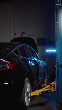 Cinematic shot of an electric car raised on a hydraulic vehicle lift inside a modern auto repair shop. Professional automotive service and maintenance concept with dark moody atmosphere