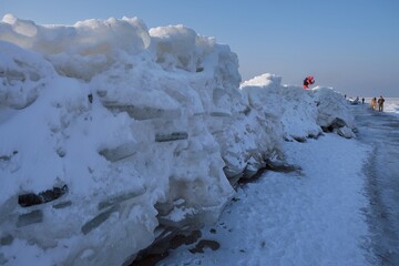 Ice toros (mountains of piled-up ice) on the beach in Mikoszewo, Baltic Sea, Pomerania, Poland. This is a very interesting and rare phenomenon. Little silhouettes of walking people.