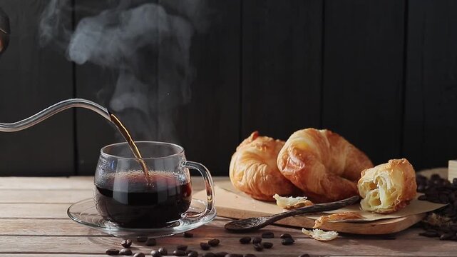 The slow-motion video shows hot coffee being poured into a cup, steam rising. Roasted coffee beans and bread are placed on the table. This video was shot with a digital camera and edited by colleagues