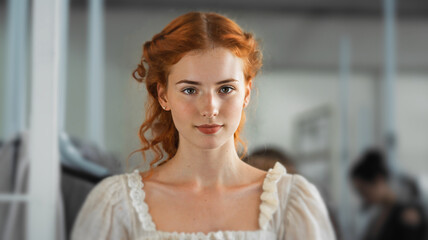 red hair woman in the past with vintage period hairstyle wearing elegant white dress with lace ruffles standing in a historical classical interior setting with antique furniture.