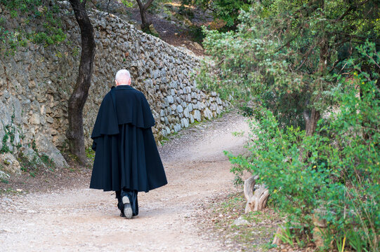 Catholic priest wearing a traditional black cassock walking alone on a forest path near Cotignac, southern France, close to a historic religious site associated with Saint Joseph