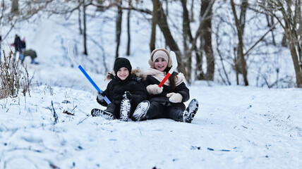 Two happy children with hockey sticks sitting in the snow during winter playtime