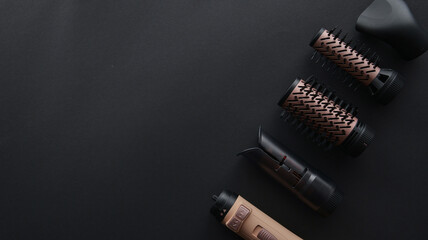 Modern hair styling tools with interchangeable attachments laid out on a dark background