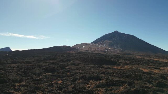 Volcanic peak under a clear sky. Foreground is rough, dark lava field.