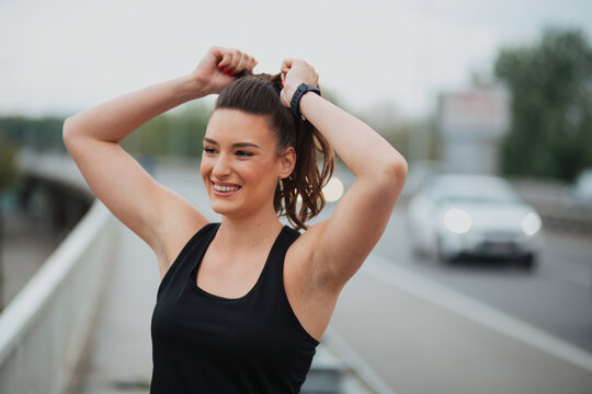 Young female runner tying her hair in a ponytail while preparing for an outdoor workout in the city.