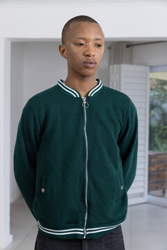 African American man standing at home hands behind back in jacket ring-pull zipper by louvered door