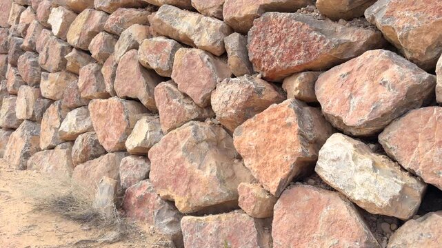Closeup pan shot of dry stack wall construction for retaining soil and stone material in arid environment of rugged desert terrain