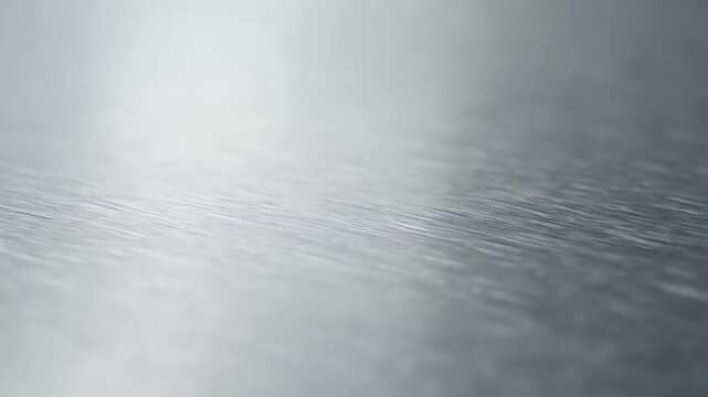 Abstract macro shot of subtle water ripples or liquid surface texture in soft silver and cool grey tones, creating a tranquil, reflective background.