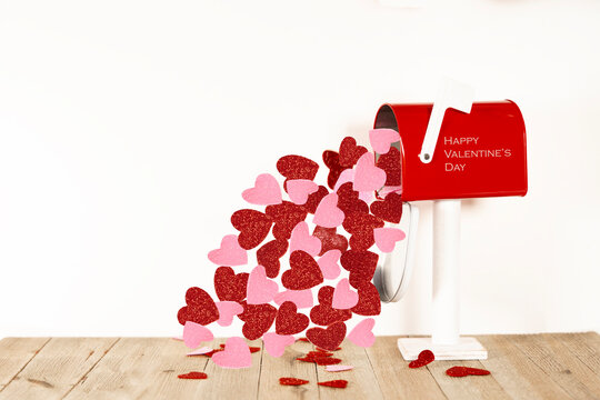 A red Valentine's Day mailbox with red and pink hearts flowing out of it on a white blank background for text.  No people are in this photo.