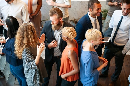 Diverse group at a social event, mingling and networking. People in business attire, engaging in conversation, holding drinks, and smiling in a lively atmosphere. Diverse people talking together.