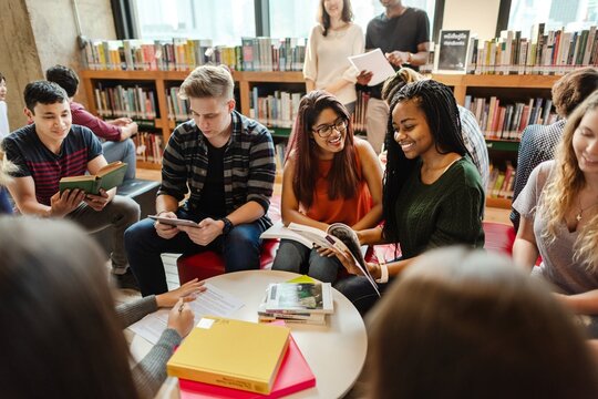 Diverse group of young adults studying in a library. Students reading books, discussing, and collaborating. Engaged in learning, sharing ideas, and teamwork. Diverse people in library.