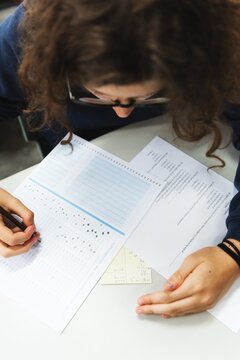 Person taking a test, focused on filling answers. Test, answers, and focus are key. Writing on paper, test-taking scene, and concentration are evident. School exams. Education and knowledge.