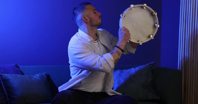 Man playing tambourine in blue light at home