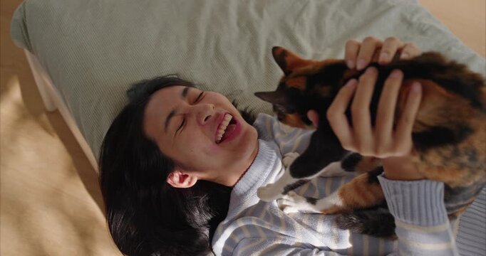 Happy Young Asian Woman Playing with Calico Cat in Sunny bedroom - Lifestyle and Pet Ownership Concept	