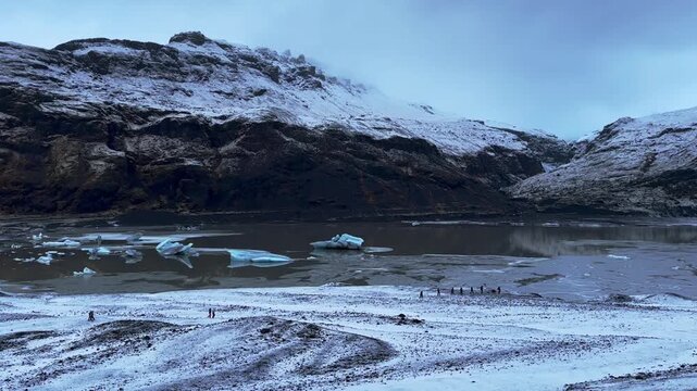 Static Shot of S&oacute;lheimaj&ouml;kull Glacier Lagoon, Icebergs, and Hikers at Cloudy Sunrise, Iceland.