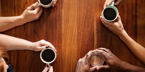 Naklejka premium Diverse group of people having coffee. Top view of hands holding coffee cups. Coffee meeting with diverse hands. Coffee and conversation among diverse group of pleple. Diverse people drinking coffee